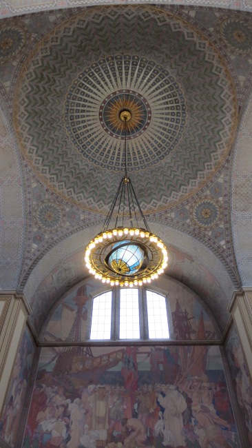An intricately painted ceiling and one panel featuring the history of California inside the rotunda of the LA Central Library. 